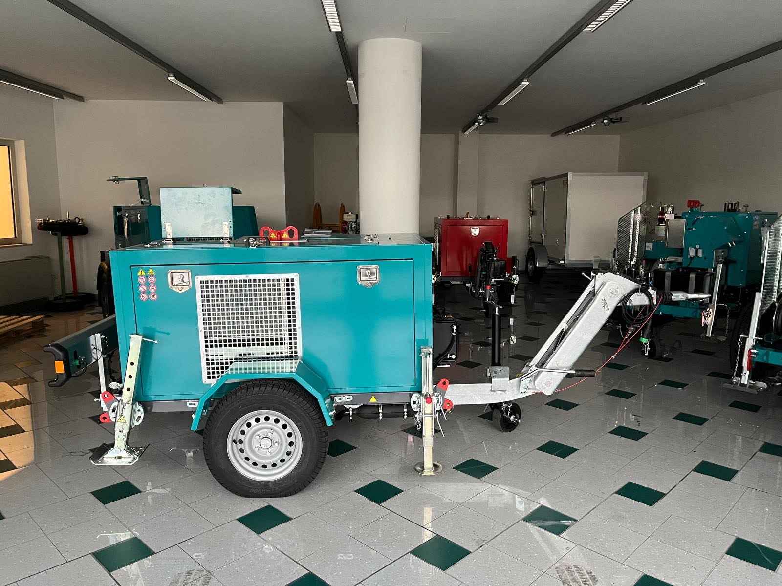 Mobiler Geräteanhänger (z. B. Kabelziehwinde/Generator) in Türkis – einachsiges Fahrgestell mit schallgedämmter Haube, Lüftungsgitter, Deichsel, Stützrad und abklappbaren Stützfüßen; präsentiert im Indoor-Showroom.