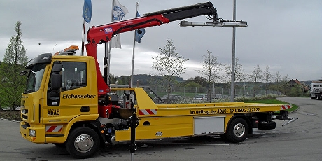 Gelber Autotransporter/Abschleppwagen mit HMF Knickarm-Ladekran und Hebebalken, ausgefahrene Abstützungen – ideal zum Verladen und Bergen von Fahrzeugen.