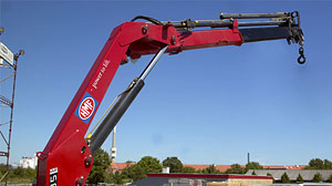 Nahaufnahme eines HMF Knickarm-Ladekrans: roter Ausleger mit Hydraulikzylinder und ausfahrbarem Teleskoparm vor blauem Himmel – robust für Verladen, Montage und Baustelleneinsatz.