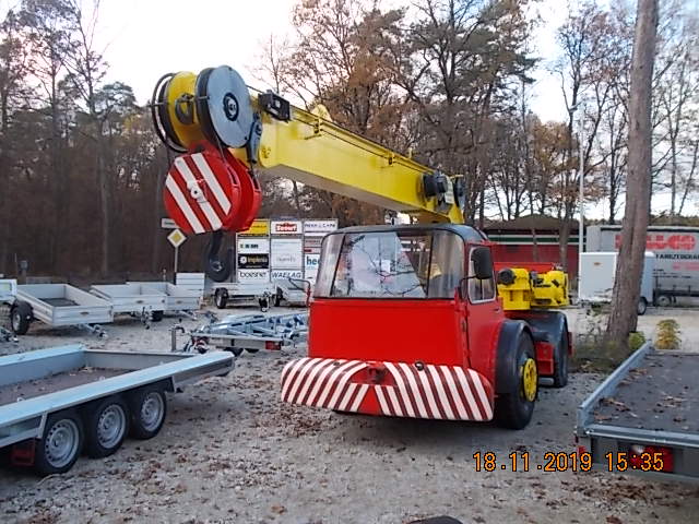 Mobiler Autokran/Teleskopkran – rotes Fahrerhaus, gelber Teleskopausleger und große rot-weiß gestreifte Hakenflasche; ideal für Hebe-, Verlade- und Montagearbeiten, Aufnahme auf dem Betriebshof.