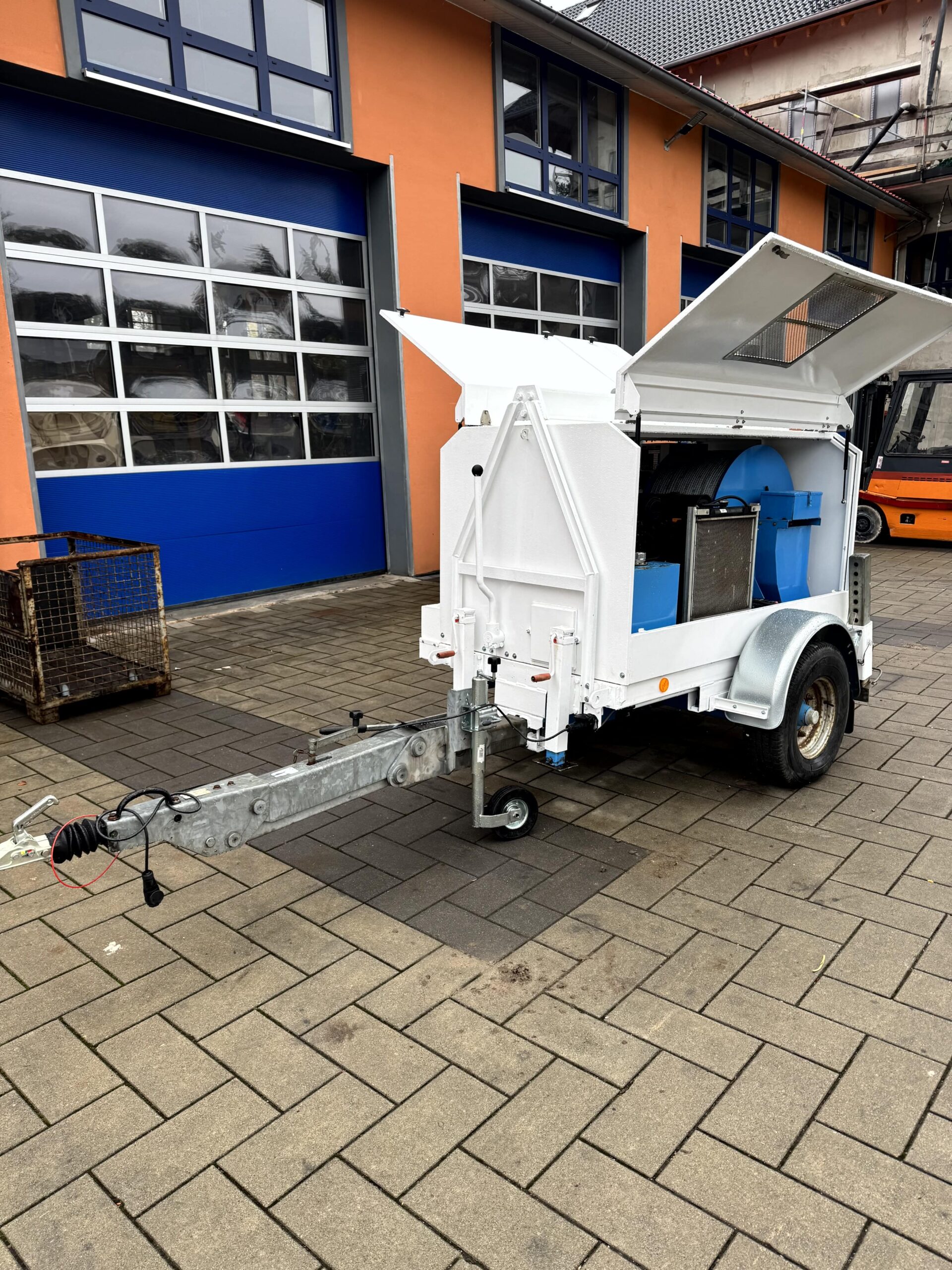 Mobiler Geräte-/Serviceanhänger auf Einachse – weißes, schallgedämmtes Gehäuse mit seitlich und oben geöffneten Klappen, Deichsel und Stützrad; ideal als Generator-, Kompressor- oder Hydraulikaggregat für Baustellen.