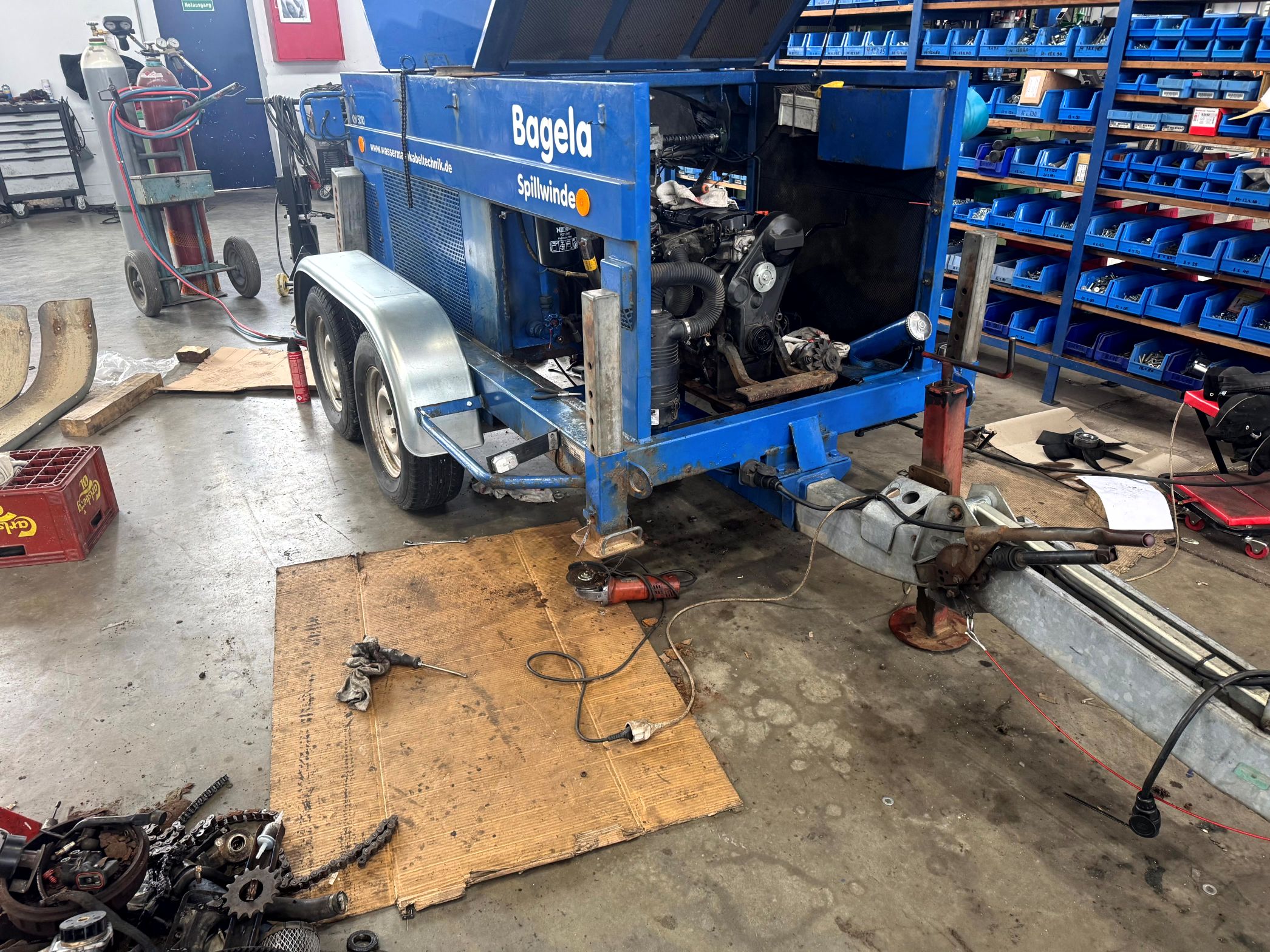 Bagela Spillwinde/Kabelziehwinde auf Trailer in der Werkstatt – geöffnete Haube mit sichtbar eingebautem Motor, Deichsel und Stützfuß; Wartung/Reparatur der Kabelzuganlage.