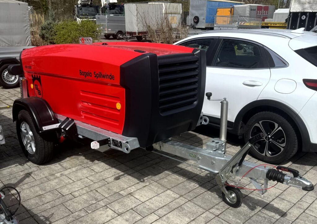 Bagela Spillwinde/Kabelziehwinde – trailer-montierte, schallgedämmte Einheit in Rot auf Einachs-Fahrgestell mit Deichsel, Auflaufbremse und Stützrad; mobile Lösung für Kabelzug im Leitungsbau.